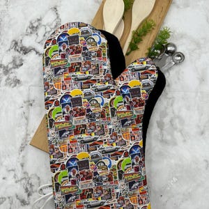 May include: A white oven mitt with a black trim and a colorful collage of Back to the Future movie images and text, including the DeLorean time machine, Marty McFly, and the iconic "OUTATIME" clock.