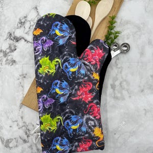 May include: A black oven mitt with a colorful dragon pattern. The dragons are flying in a starry sky. The mitt has a white loop for hanging.