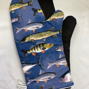 Peut inclure: Un gant de cuisine avec un motif de poissons sur fond bleu. L'intérieur est noir. Une boucle de cordon blanche est attachée sur le côté. Les poissons sont dans des tons de jaune, vert et argent.