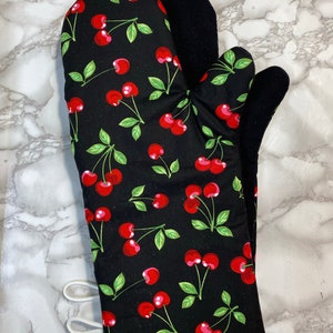 May include: Black oven mitt with a red cherry pattern. The mitt has a white loop for hanging.