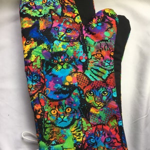 May include: A colourful oven mitt with a pattern of cats in a rainbow of colours. The cats are surrounded by colourful paint splatters.