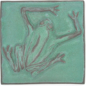 May include: A square ceramic tile featuring a raised relief design of a frog in a dark brown color against a textured, matte seafoam green background. The frog is depicted in a sprawling position with its limbs extended toward the corners of the tile.
