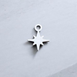 May include: A silver charm in the shape of a star with a loop at the top. The star has eight points.