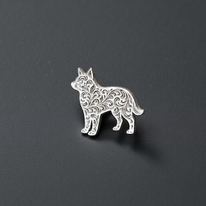Puede incluir: Un broche plateado con forma de perro con intrincados adornos florales. El broche es una representación detallada de un perro, de pie con la cabeza levantada y la cola ligeramente curvada. El broche es probablemente de metal.