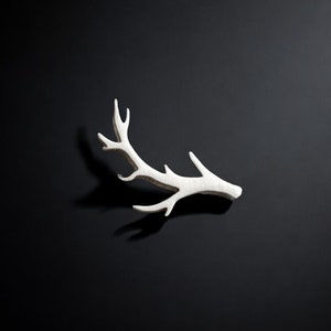 May include: A white, wooden, deer antler cutout against a black backdrop.