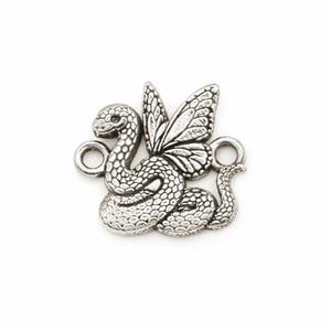 Pode incluir: Um pingente de metal prateado representando uma cobra enrolada com escamas detalhadas e uma asa de borboleta nas costas. O pingente inclui dois aros circulares nos lados opostos para fixação e apresenta um acabamento envelhecido.