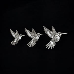 Könnte beinhalten: Drei silberne Kolibri-Wanddekorationen in verschiedenen Größen. Die Kolibris sind im Flug mit ausgebreiteten Flügeln.