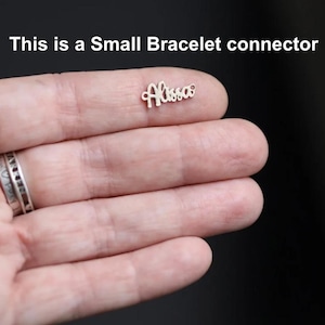 May include: A small, silver bracelet connector with the name "Alissa" in cursive script. The text "This is a Small Bracelet connector" is above the connector. The connector is held in a person's hand.