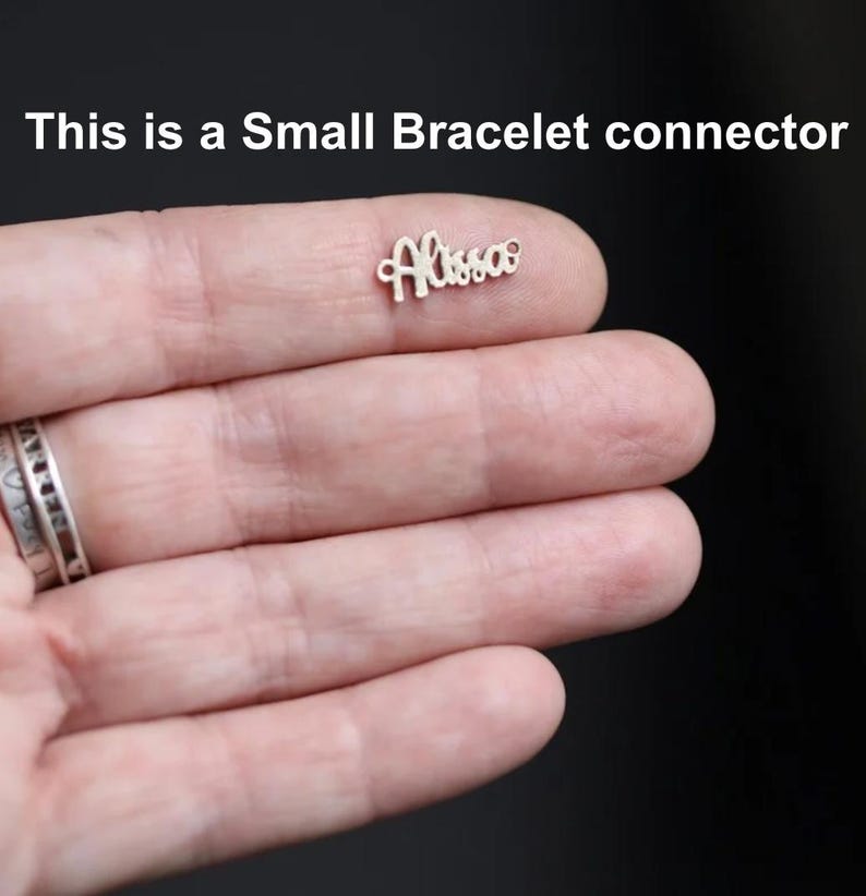 May include: A small, silver bracelet connector with the name "Alissa" in cursive script. The text "This is a Small Bracelet connector" is above the connector. The connector is held in a person's hand.