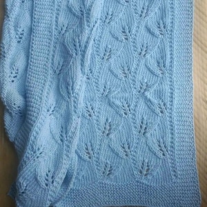 Puede incluir: Una manta de bebé de punto azul claro con un patrón de hojas.