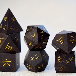 May include: Four black wooden dice with gold markings. The dice are in the shape of a pyramid, a dodecahedron, an octahedron, and a cube. The dice are stacked on top of each other.
