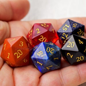 May include: Five 20-sided dice in different colors and materials. The dice are red, blue, black, and orange. The dice are all polyhedral and have gold numbers.
