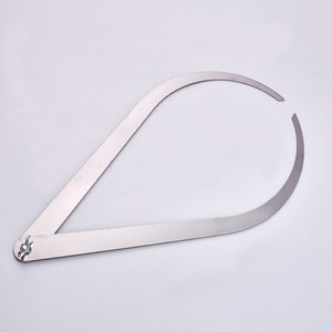 Puede incluir: Un compás de metal plateado con un brazo articulado. El compás se utiliza para medir la circunferencia de los objetos.