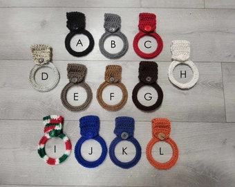 May include: Twelve crocheted dish towels with button closures in various colors, including black, gray, red, white, brown, beige, blue, orange, green, and red and white stripes. The towels are labeled with letters A through L.