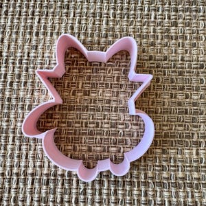 Puede incluir: Cortador de galletas de plástico rosa en forma de gato de dibujos animados con una amplia sonrisa y ojos grandes.