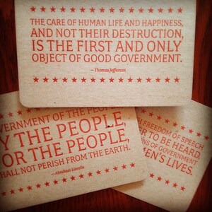Puede incluir: Tres tarjetas rectangulares de color tostado con esquinas redondeadas, cada una con texto rojo y bordes de estrellas rojas. La tarjeta superior muestra una cita de Thomas Jefferson. Las tarjetas inferiores muestran citas de Abraham Lincoln.