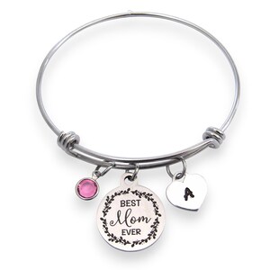 May include: Silver-toned bangle bracelet with three charms. One charm is a pink gemstone, another is a heart with the letter "A", and the third is a round charm with the words "Best Mom Ever" surrounded by a floral design.