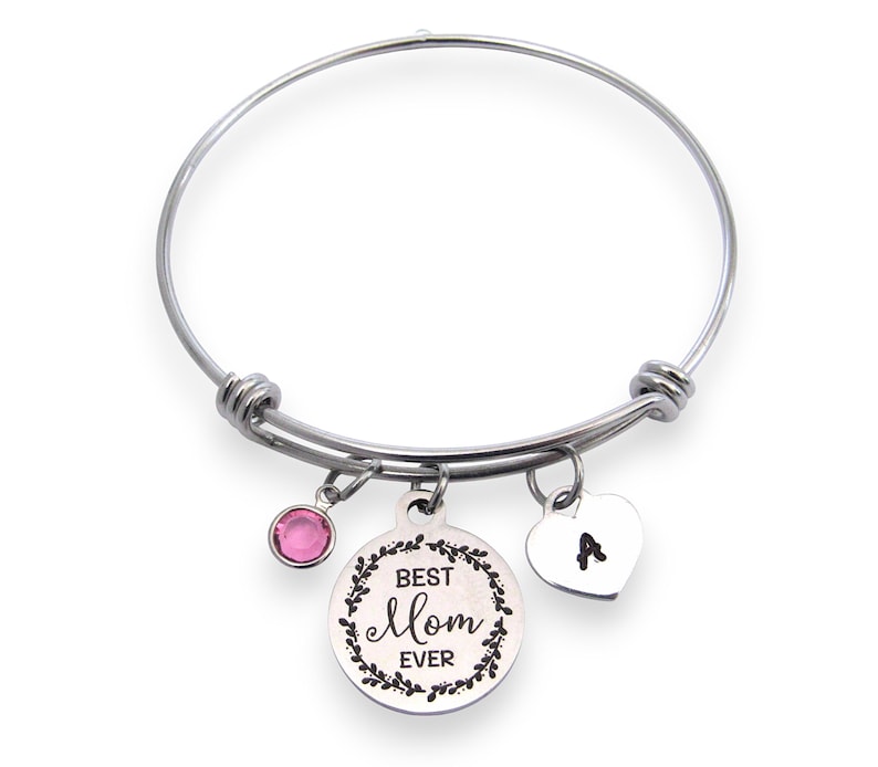 May include: Silver-toned bangle bracelet with three charms. One charm is a pink gemstone, another is a heart with the letter "A", and the third is a round charm with the words "Best Mom Ever" surrounded by a floral design.