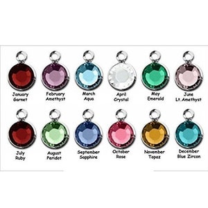 May include: A collection of twelve round gemstone charms in various colors, each with a silver-tone loop. Each charm is labeled with a month and corresponding gemstone name, including Garnet, Amethyst, Aqua, Crystal, Emerald, and Ruby.