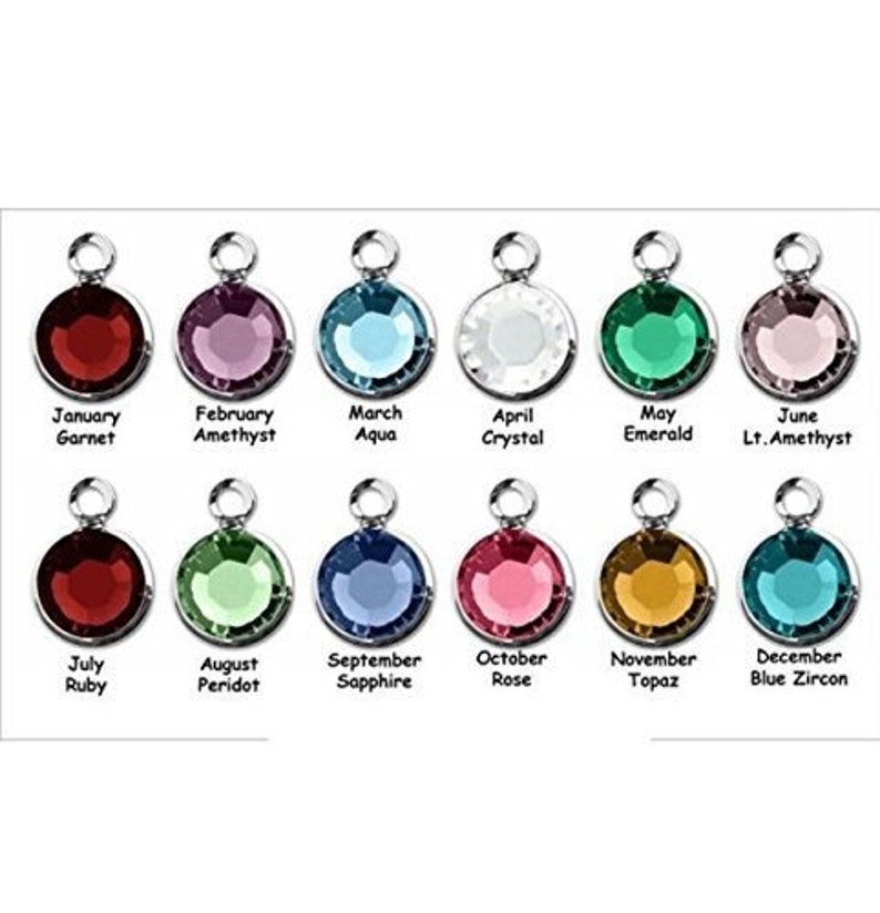 May include: A collection of twelve round gemstone charms in various colors, each with a silver-tone loop. Each charm is labeled with a month and corresponding gemstone name, including Garnet, Amethyst, Aqua, Crystal, Emerald, and Ruby.