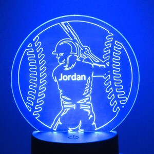 May include: A blue LED night light shaped like a baseball with a baseball player silhouette holding a bat. The player's jersey has the name "Jordan" printed on it.
