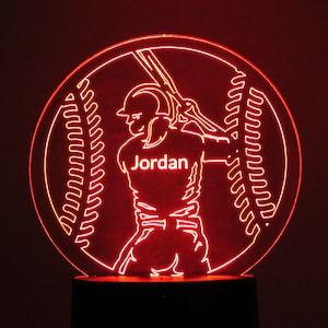May include: Red illuminated baseball night light with a baseball player silhouette holding a bat and the name "Jordan" on the jersey.
