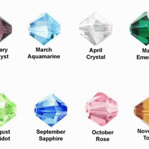 May include: A collection of twelve faceted bicone beads arranged in two rows, each labeled with a month and corresponding gemstone name: January Garnet, February Amethyst, March Aquamarine, April Crystal, May Emerald, June Light Amethyst, July Ruby, August Peridot, September Sapphire, October Rose, November Topaz, and December Blue Zircon.