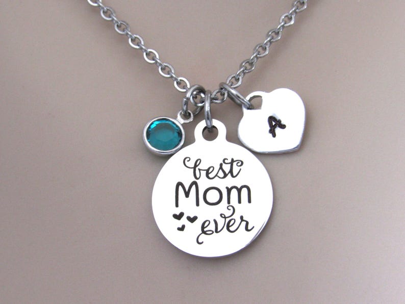 May include: Silver necklace with a round charm that says "best mom ever" with three small hearts, a heart charm with the letter "A" and a teal blue crystal charm.