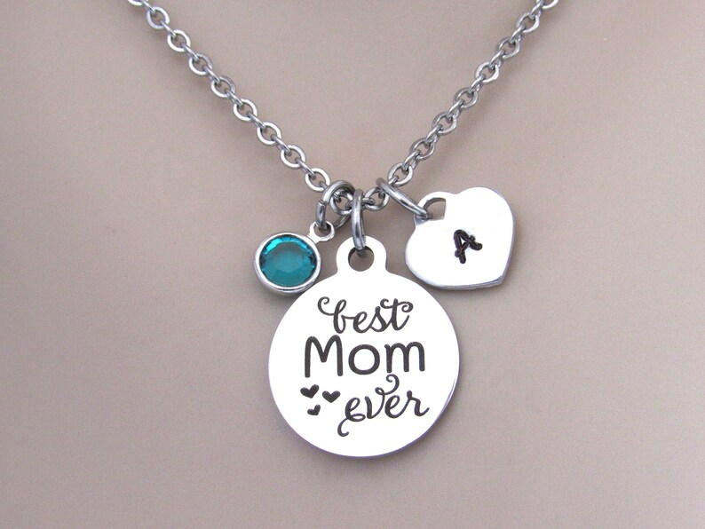 May include: Silver necklace with a round pendant that says "best Mom ever" with two small hearts, a teal blue crystal charm, and a heart charm with the letter "A" engraved on it.
