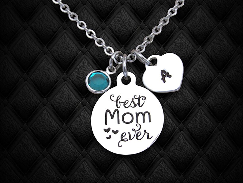 May include: Silver necklace with a round charm that says "best mom ever" with three small hearts, a teal blue crystal charm, and a heart charm with the letter "A" engraved on it.