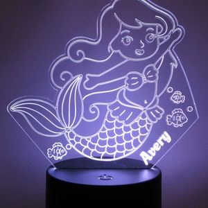 May include: A white acrylic night light shaped like a mermaid with a fishtail, a bow, and long hair. The mermaid is surrounded by three small fish. The name "Avery" is written on the base of the night light.