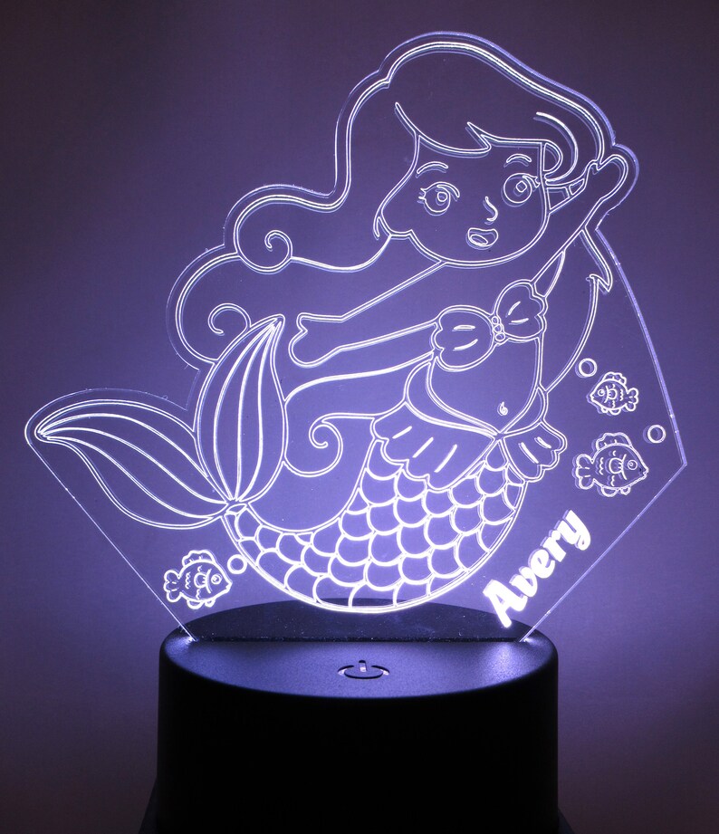 May include: A white acrylic night light shaped like a mermaid with a fishtail, a bow, and long hair. The mermaid is surrounded by three small fish. The name "Avery" is written on the base of the night light.