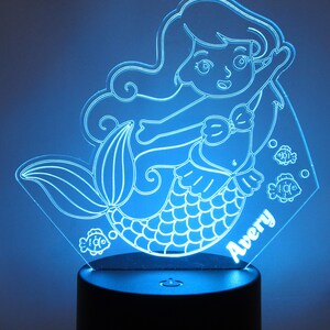 May include: A blue light-up nightlight featuring a mermaid with a tail, a seashell bra, and long flowing hair. The mermaid is surrounded by small fish. The nightlight has a personalized name, "Avery", at the bottom.