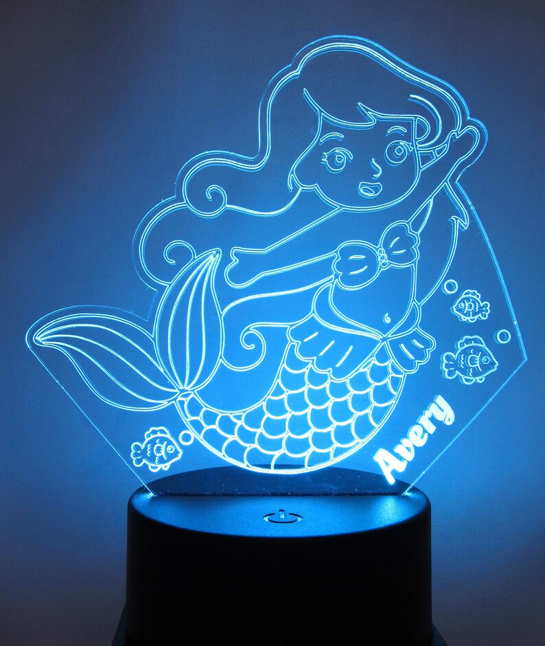 May include: A blue light-up nightlight featuring a mermaid with a tail, a seashell bra, and long flowing hair. The mermaid is surrounded by small fish. The nightlight has a personalized name, "Avery", at the bottom.