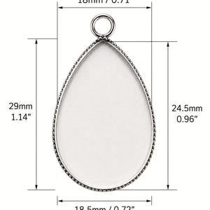 May include: A silver-toned teardrop-shaped pendant tray with a smooth white center and a small circular bail at the top. The pendant measures 0.71 inches wide by 1.14 inches tall, with an inner area of 0.72 inches wide by 0.96 inches tall.