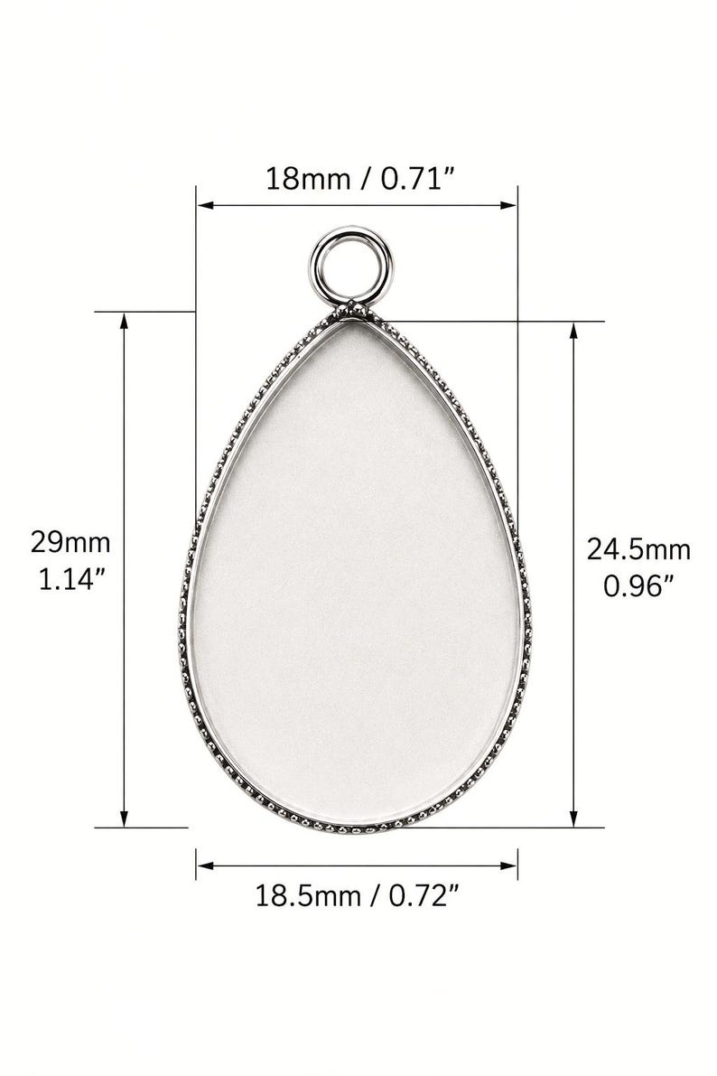 May include: A silver-toned teardrop-shaped pendant tray with a smooth white center and a small circular bail at the top. The pendant measures 0.71 inches wide by 1.14 inches tall, with an inner area of 0.72 inches wide by 0.96 inches tall.