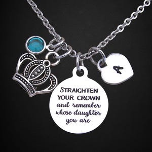 May include: Silver-toned necklace with multiple charms. Includes a crown, a heart with the letter "A", a teal-colored gem, and a circular charm with the text "STRAIGHTEN YOUR CROWN and remember whose daughter you are."