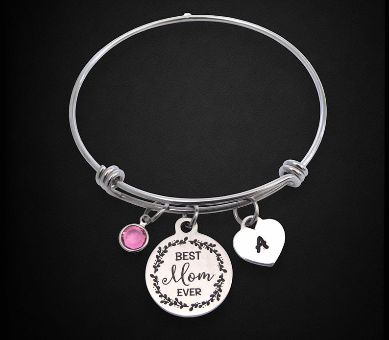 May include: Silver-toned bangle bracelet with three charms. One charm is a pink gemstone, another is a round pendant with the text "Best Mom Ever" and a floral border, and the third is a heart-shaped charm with the letter "A".
