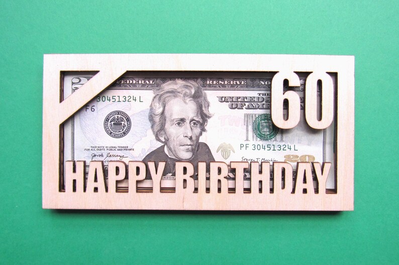 May include: A wooden card with a cutout for a dollar bill. The bill is visible through the cutout and the number "60" is cut out of the wood above the bill. The words "Happy Birthday" are cut out of the wood below the bill.
