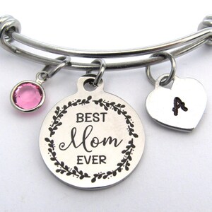 May include: A silver-toned expandable bracelet with three charms. One charm is a pink gemstone, another is a round pendant with "BEST Mom EVER" in a wreath, and the third is a heart with the letter "A".