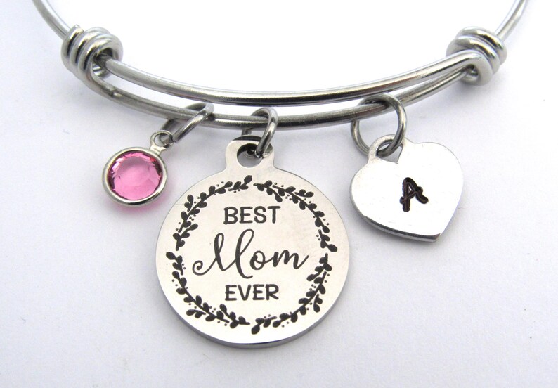 May include: A silver-toned expandable bracelet with three charms. One charm is a pink gemstone, another is a round pendant with "BEST Mom EVER" in a wreath, and the third is a heart with the letter "A".