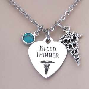 May include: A silver necklace with a heart pendant that says "Blood Thinner" and a medical symbol. The necklace also has a small blue crystal charm and a larger silver medical symbol charm.