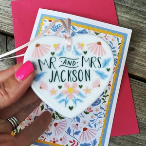 May include: White ceramic heart-shaped ornament with a floral design and the text "Mr. and Mrs. Jackson".