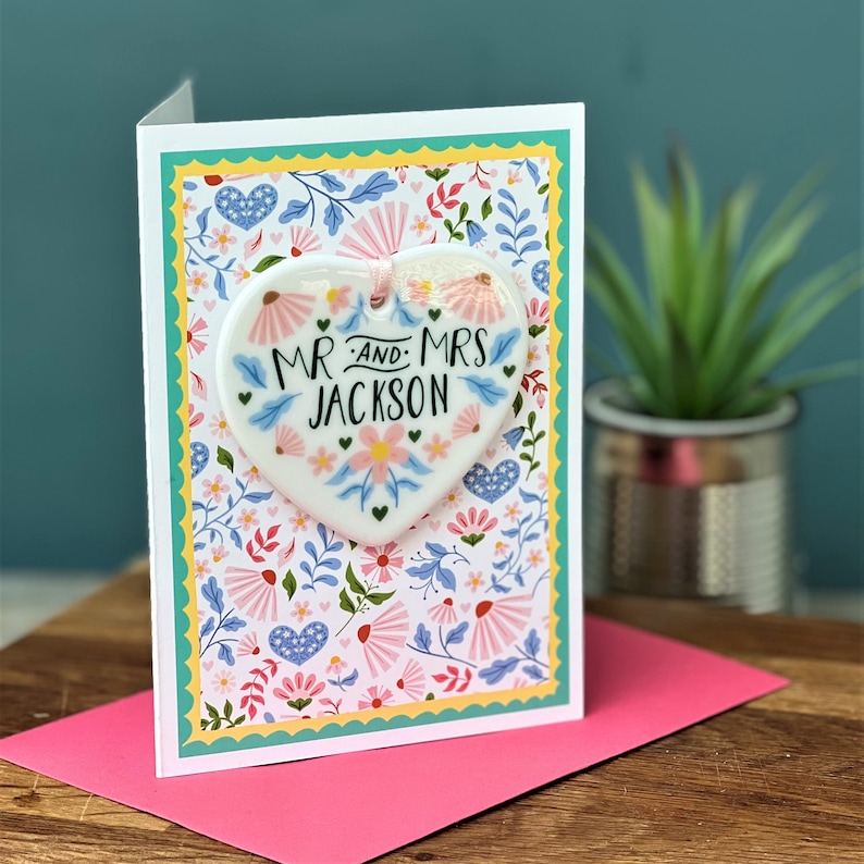 May include: A white ceramic heart ornament with a floral design and the text "Mr. and Mrs. Jackson" on a card with a floral pattern.