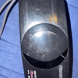 K&ouml;nnte beinhalten: Schwarze Canon Sure Shot 70 Zoom Kamera mit grauem Gurt. Die Kamera hat ein gro&szlig;es Objektiv und die W&ouml;rter "SURE SHOT 70 Zoom" und "DATE AOF" sind auf der Vorderseite aufgedruckt. Die Kamera ist rechteckig mit abgerundeten Kanten.