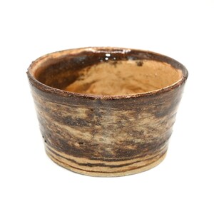 May include: A small, handmade ceramic bowl with a rustic appearance. The bowl features a cylindrical shape with a slightly flared rim. The exterior has a textured, marbled effect in shades of brown and tan. The interior is a lighter tan color.