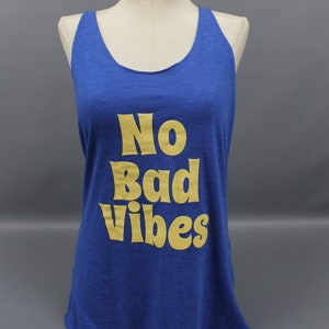 May include: Blue tank top with the text "No Bad Vibes" in gold lettering. The sleeveless top is displayed on a mannequin. The shirt has a scoop neck and a relaxed fit, suitable for casual wear.