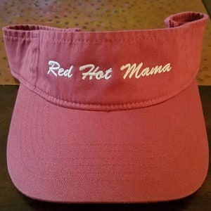 May include: A red visor with white embroidery that reads "Red Hot Mama".