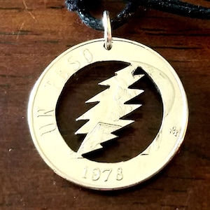 May include: Silver-colored pendant necklace featuring a cut-out lightning bolt design within a circular frame. The pendant is made from a coin, with the year 1978 visible. The necklace hangs on a black cord.