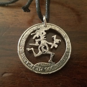 May include: A silver coin necklace with a cutout design of a jester figure. The coin is a Mexican 50 centavos coin with the text "ESTADOS UNIDOS MEXICANOS" around the edge.